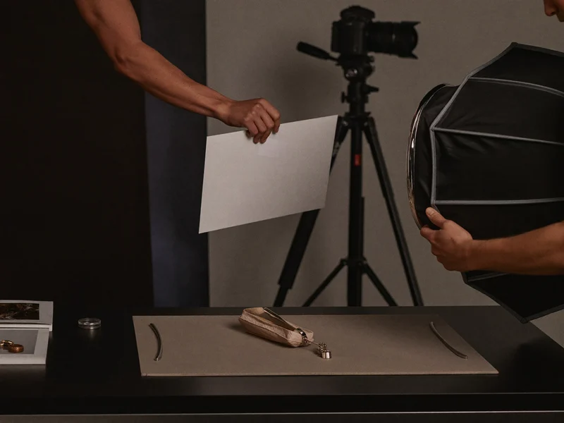 Ruce nastavující odrazku vedle softboxu u stolní sestavy, v pozadí fotoaparát na stativu
